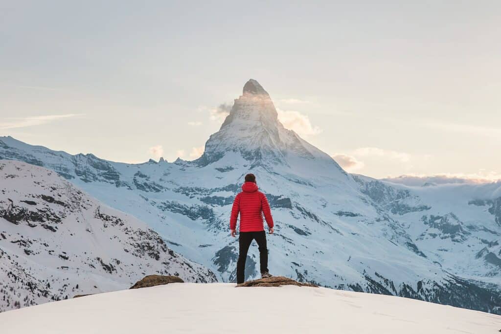 person in red hoodie standing on snowy mountain during daytime